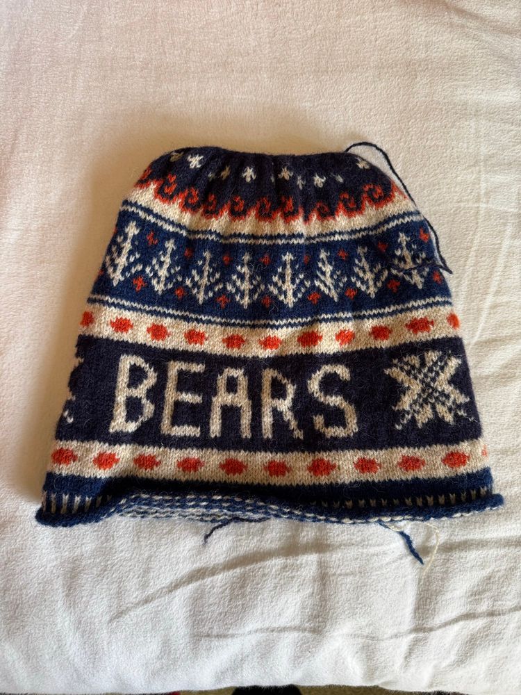 An unfinished Shetland style hat in blue, orange and white fair isle. This side says Bears.