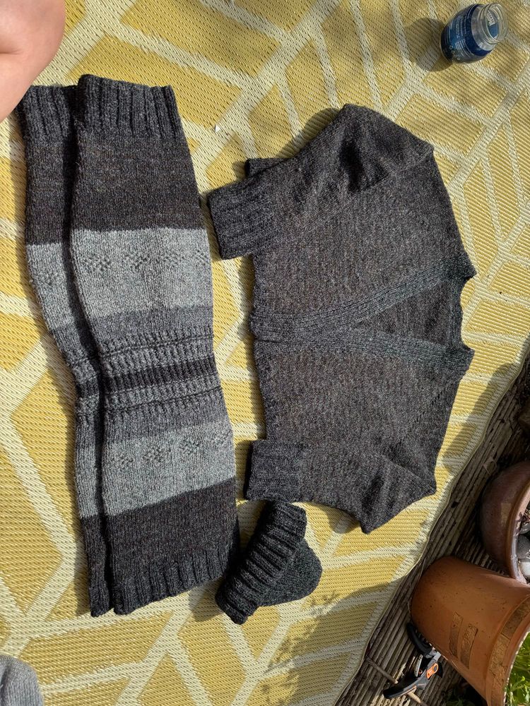 A photo of a cardigan, huge leg warmers and a beanie- knitted up in rough wool in shades of dark and light grey and dark green. 