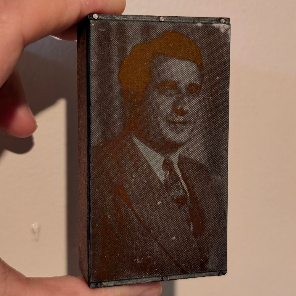 a halftone print block photo of a man with a suit and tie on. physically it is some type of metal that is about the thickness of a quarter, and nailed to a small block of wood