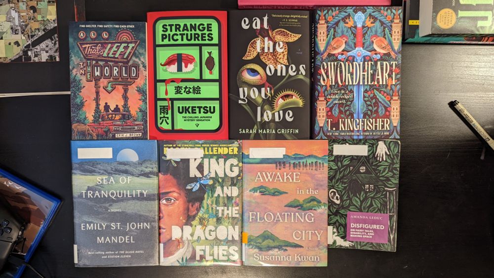 eight books placed on a table, all of which meet the prompt criteria to various degrees, most of which also satisfy one of the two bonus prompts (lgbtqia2+ author or characters, themes of isolation). titles: All That's Left in the World by Erik J. Brown, Strange Pictures by Uketsu, Eat the Ones You Love by Sarah Maria Griffin, Swordheart by T. Kingfisher, Sea of Tranquility by Emily St. John Mandel, King and the Dragonflies by Kacen Callender, Awake in the Floating City by Susanna Kwan, and Disfigured: On Fairy Tales, Disability, and Making Space by Amanda Leduc.