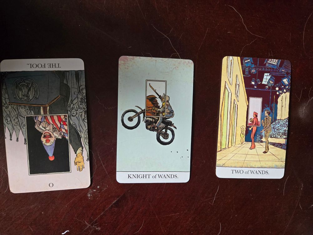 Three cards from the Unveiled Tarot deck: the fool (reversed), knight of wands, two of wands