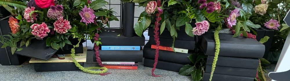 A closeup of the base of a large floral art piece showing some of the banned books in color amongst blank black volumes.