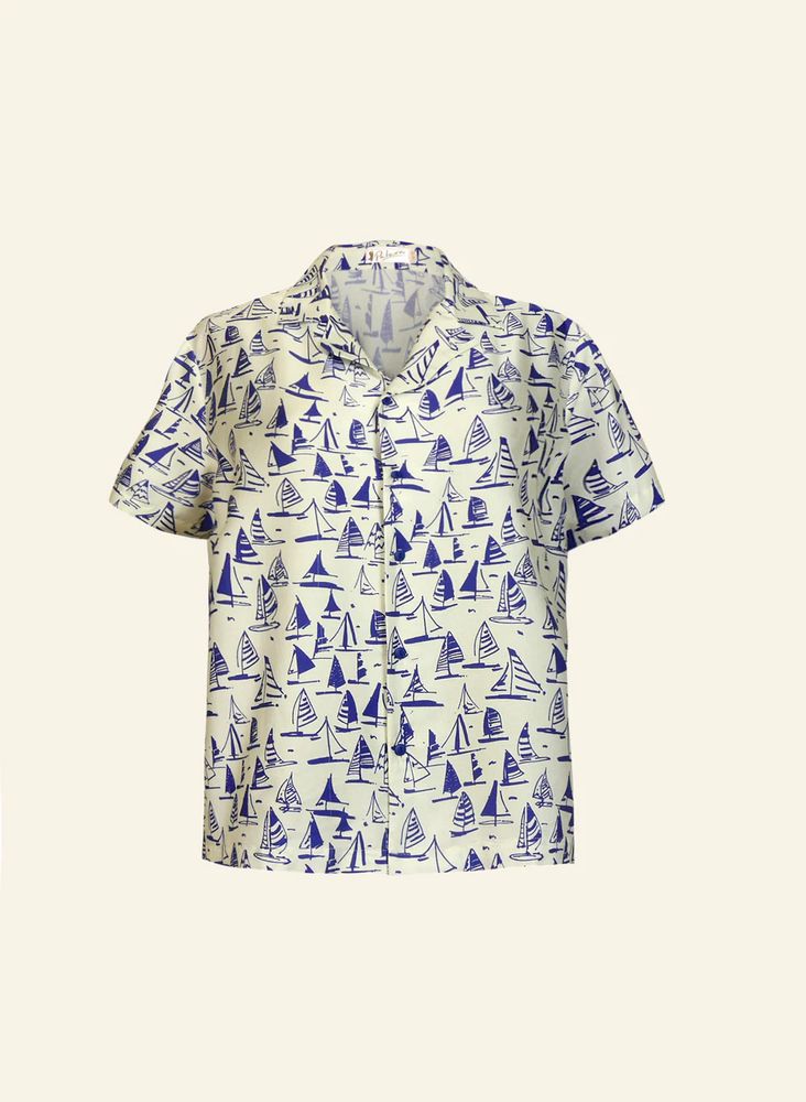 A white, short sleeve, button down shirt with an armada adornment of small blue sailboats