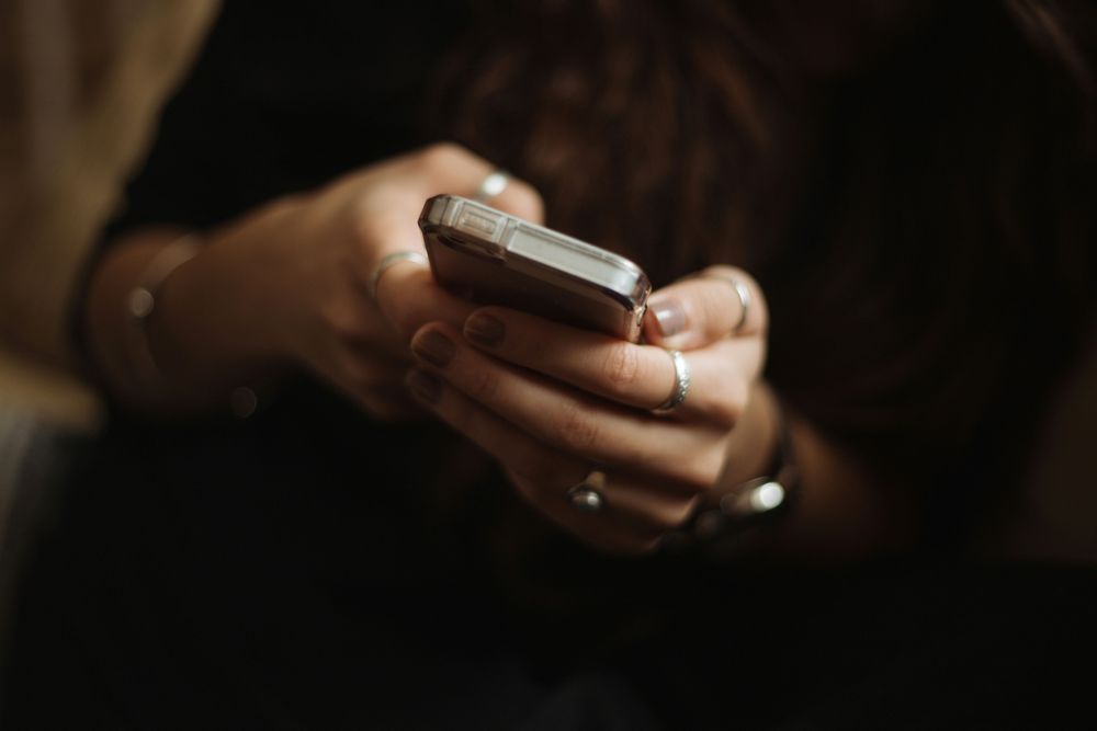 Person holding phone towards camera with a black background.