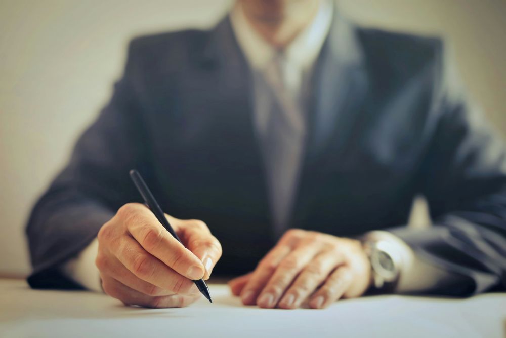 A close up of an individual in a suit signing a document.