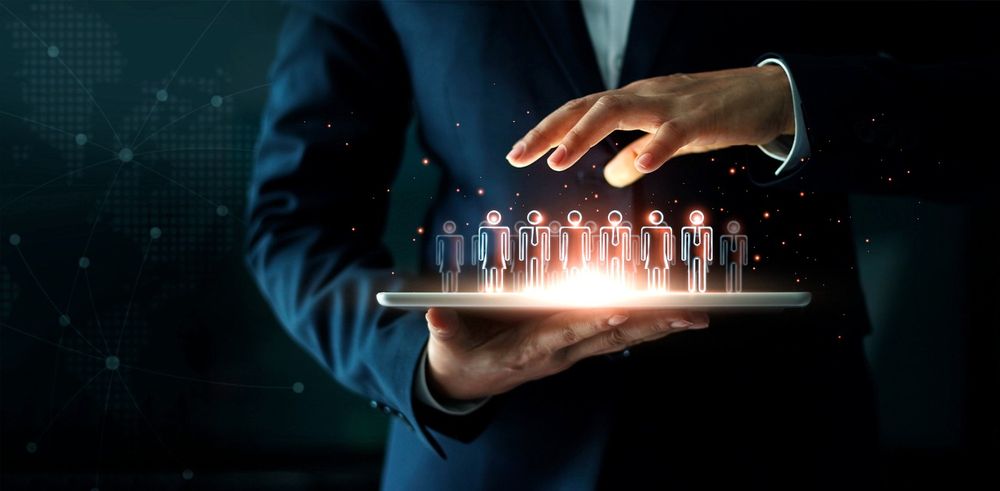 This image shows a man in a suit holding a tablet which has little people figures projecting from the tablet.