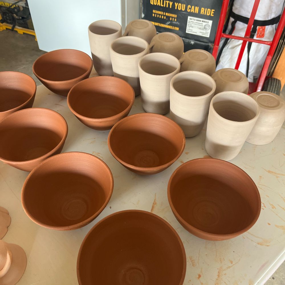 Wheel thrown bowls, pint glasses, and mugs drying on a table