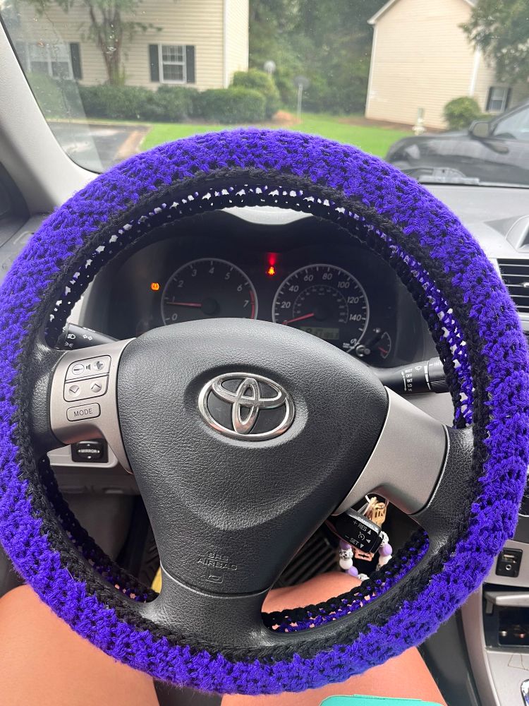 royal purple steering wheeel cover with black rim crochet on car wheel. 