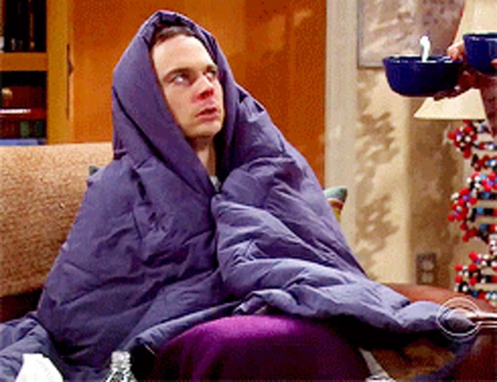 a man wrapped in a purple blanket sits on a couch