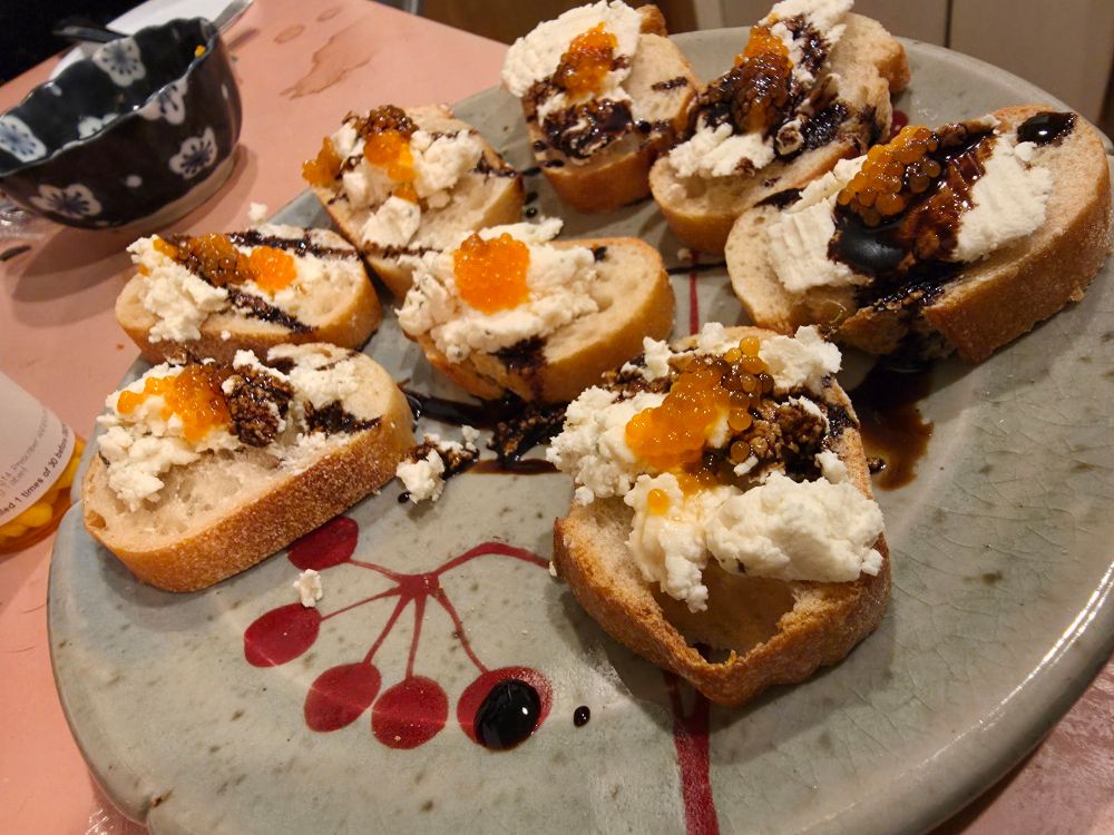 A plate of little bread slices topped with goat cheese, trout caviar, and a drizzle of balsamic vinegar.