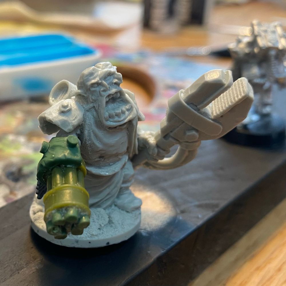 A miniature post-apocalyptic sci-fi mutant figure with a metal claw hand, three eyes, and a Gatling gun arm. 