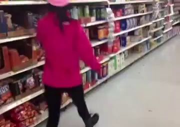 a woman in a pink jacket is walking down a aisle in a grocery store .