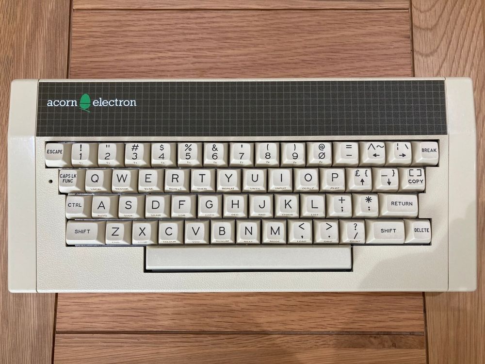 Top-down view of an Acorn Electron, a classic 1980s British home computer, featuring its beige case and full QWERTY keyboard, sat on a wooden table 