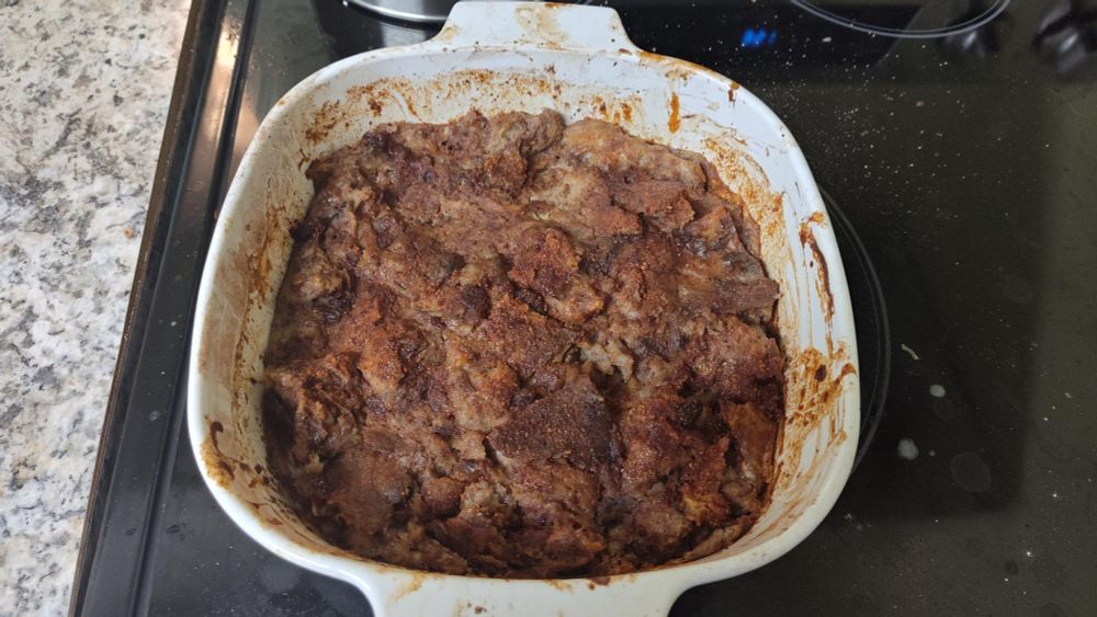 a rich brown bread pudding in a white ceramic dish, the edges are rimmed with cinnamon
