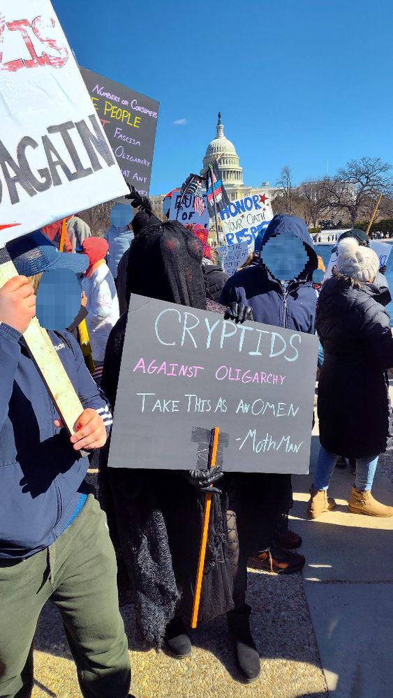 Person in black cryptid costume holding up a sign that reads 
Cryptids against oligarchy 
Take this as an omen
Mothman 