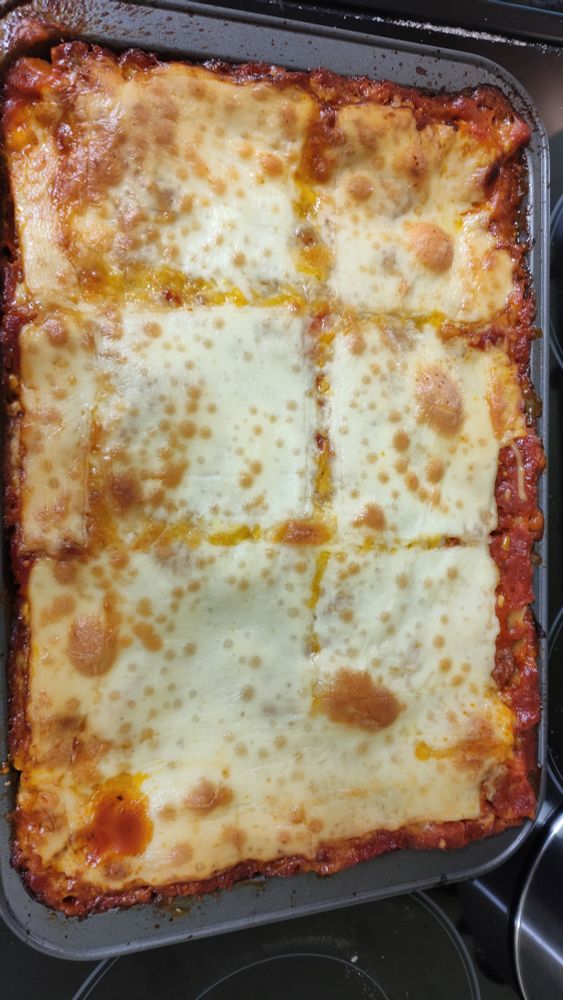A pan of lasagna. It is gooey and cheesy and melted and just a little brown with red sauce flirting at the edges 