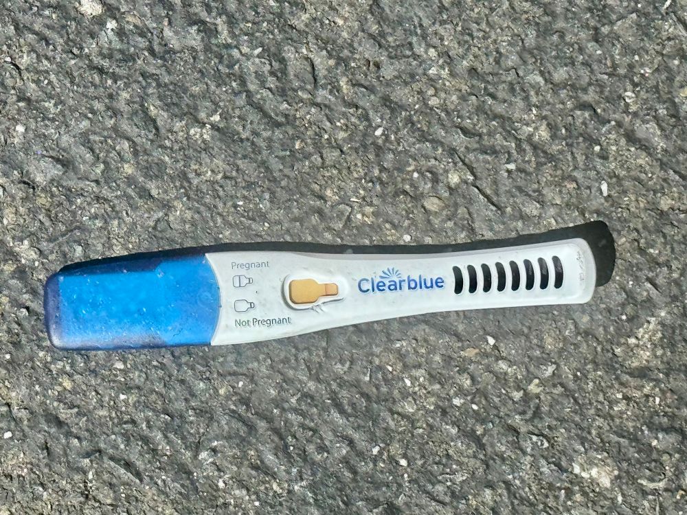 Clearblue pregnancy test that shows “not pregnant,” on asphalt, in a parking lot.