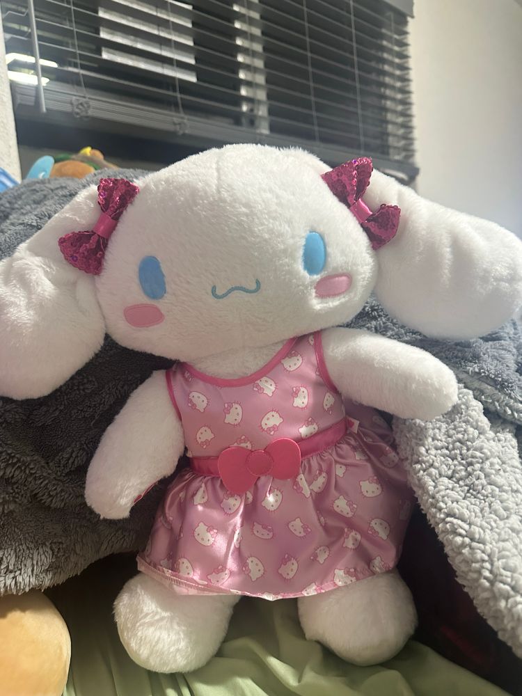 the regular cinnamoroll from build a bear wearing a light pink dress and two pink sequined bows on his ears