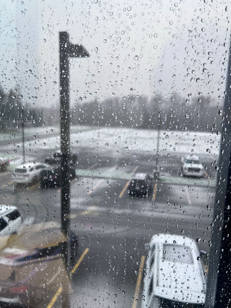 View through a wet window pane to a snowy and slushy parking lot