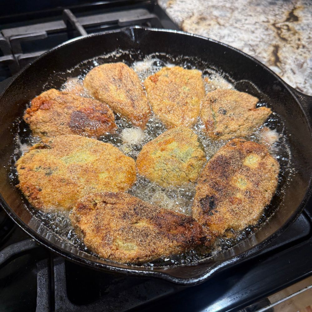 A cas iron pan with corn meal covered peppers frying.