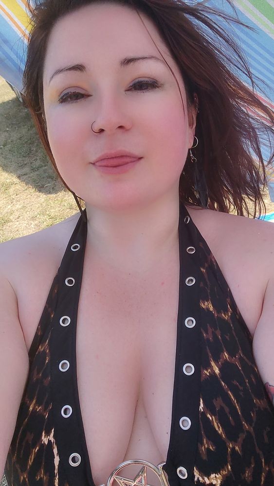 a pale #redhead femme in a leopard print bikini with an upside down pentacle centre piece sticking her tongue out at you gently. 

shes obviously at an Ontario lake beach, meaning no sand but tons of soft grass