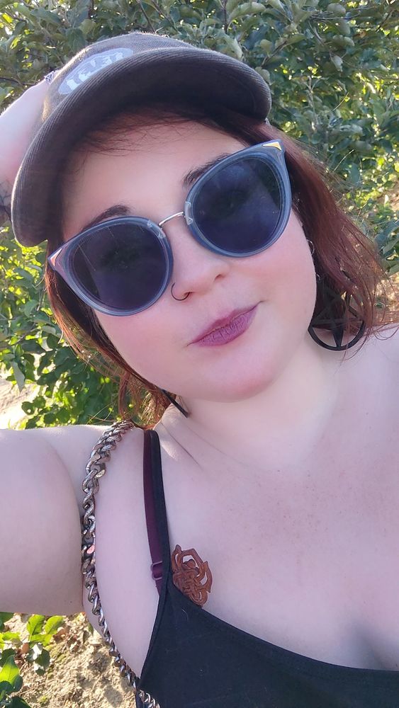 a pale chubby redhead in big blue sunglasses. she's got pale skin but very pink cheeks, forehead, and chin 
she's holding a too big baseball cap on her head