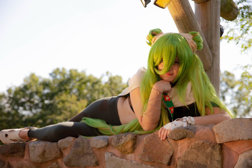 A cosplay of the Ground Type Hatsune Miku from the Pokemon Project Voltage Collaboration. She’s lying on top of a stone wall, resting her hand on one hand.