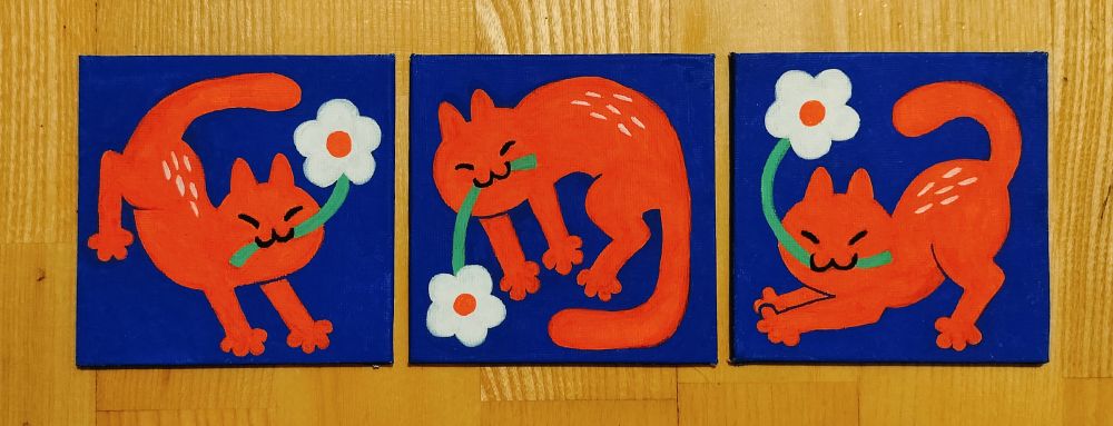 Photo of three small square paintings. They are all dark blue with simple red cats that are looking happy, eyes closed. All of them have white flowers on their mouths.