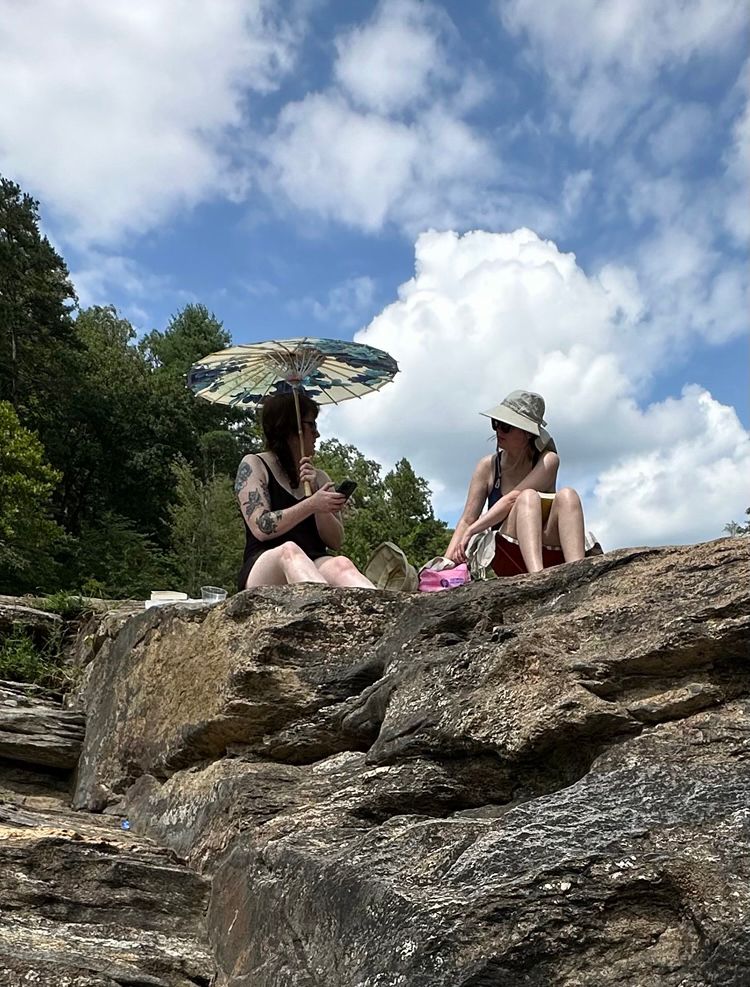 two ladies talking on sunny rocks on the bank of a river after swimming 