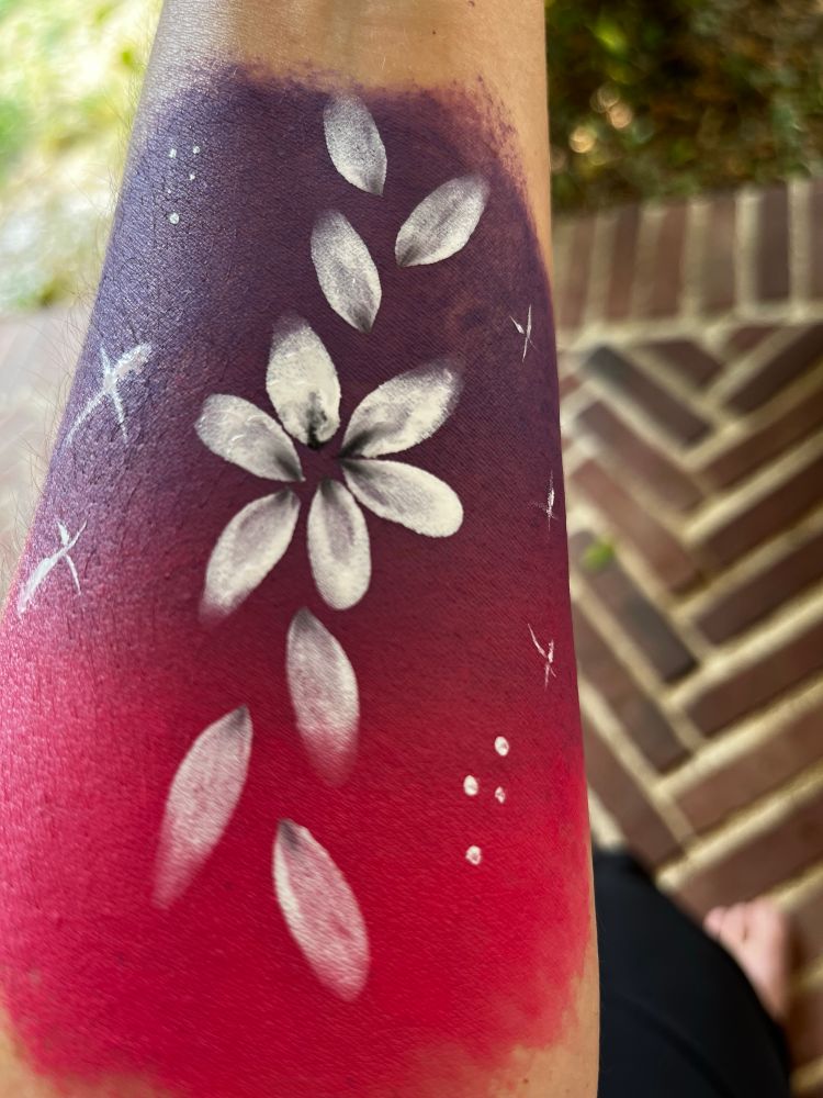 Photo de mon bras avec un maquillage : le fond est dégradé violet et rose, dessus est dessiné une fleur avec des pétales blanches