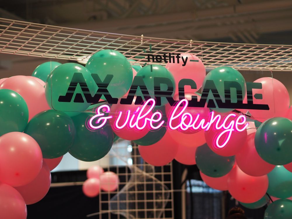 A festive arrangement of pink and teal balloons surrounding a neon sign that says "AX Arcade & Vibe Lounge," with "Netlify" subtly displayed above, creating a vibrant event setting.