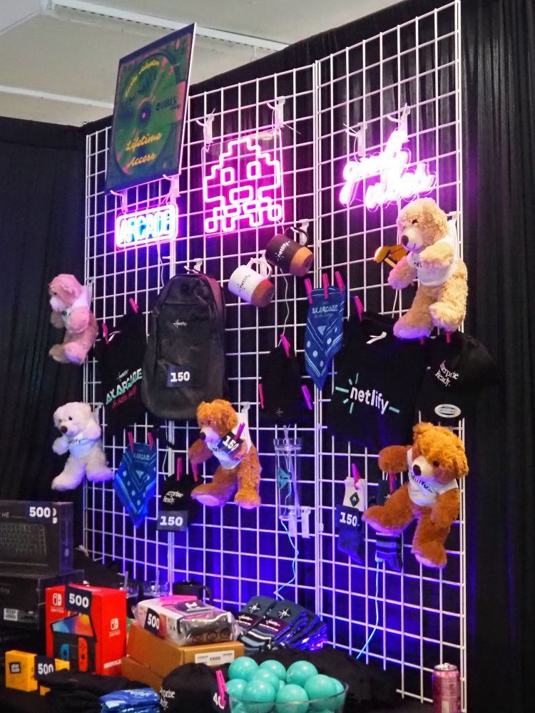 A prize display wall showcasing Netlify branded merchandise and assorted rewards, including teddy bears, neon arcade signs, coffee mugs, a backpack, and higher-value items like a Nintendo Switch, clearly labeled with point values.