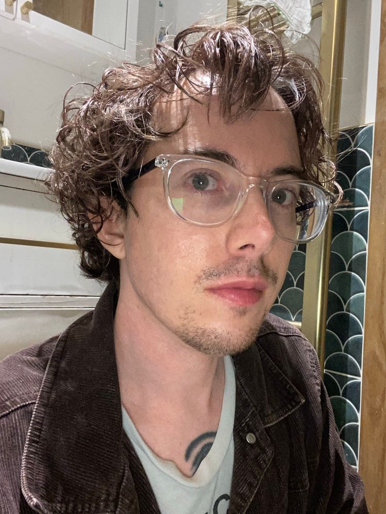 bespectacled white guy with short, gelled wavy hair