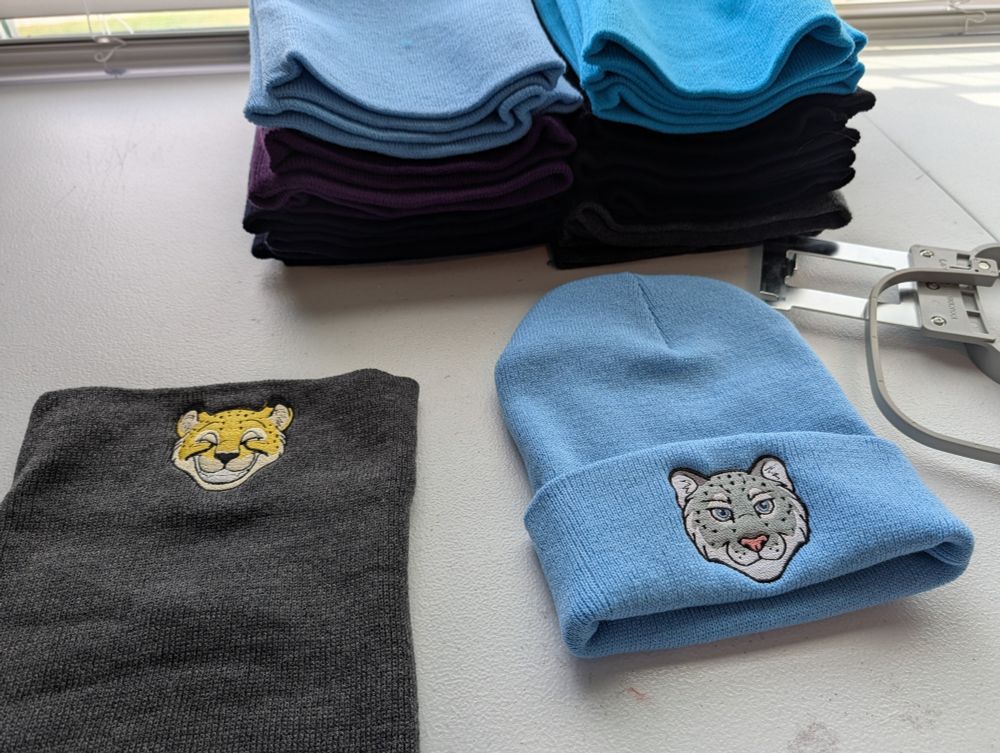 Stack of beanies in cool colors with cheetah and snow leopard embroidery