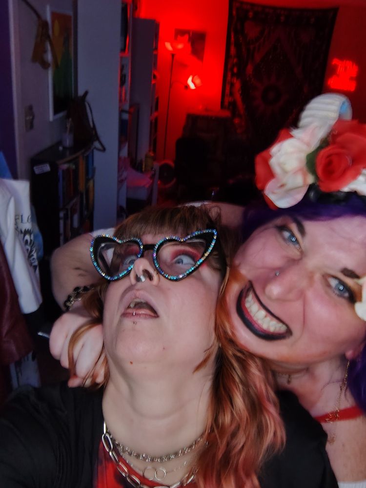 echo, wearing curling ram's horns bedecked in white & red flowers, smiles & shoves a (toy) knife into its boywife's neck, as their eyes roll back & tongue lolls out