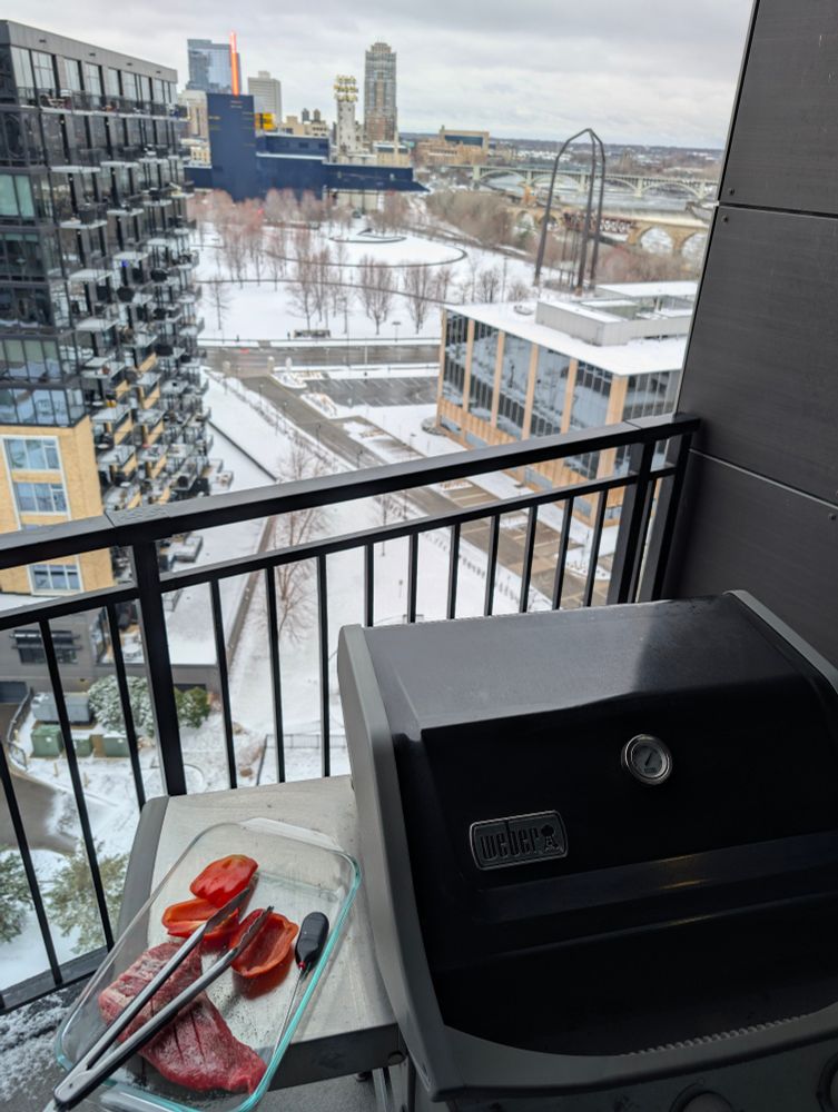 BBQ on a balcony with Minneapolis in the background. Snow covers the ground 