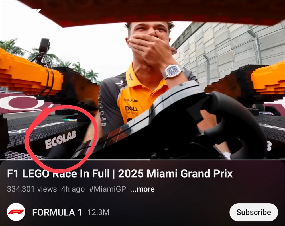A still from a YouTube video showing an internal camera view of McLaren driver Lando Norris covering his mouth and laughing as he drives a Formula 1 car made of LEGO ahead of the Miami Grand Prix. The Ecolab logo is featured prominently.