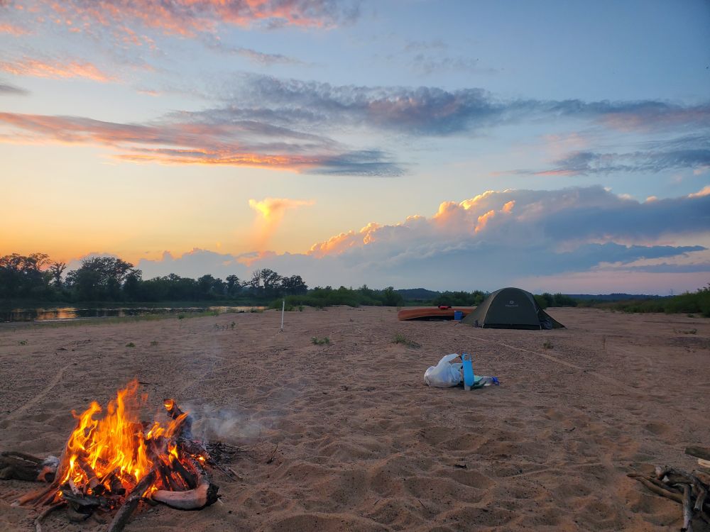 Sunset clouds with campfire and tent on a beach.