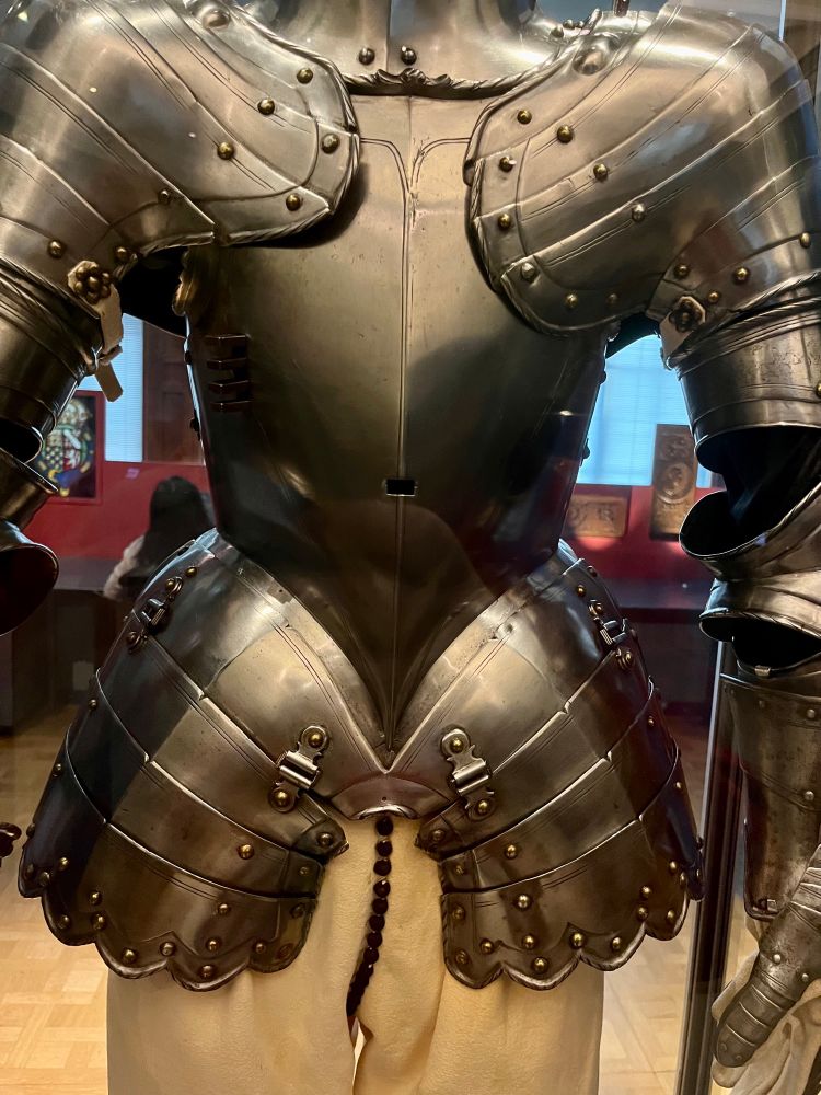 This half-armour was made for the tilt - a popular pastime for noblemen in about 1600, involving combat on horseback. Only the upper part of the body required protection. The breastplate had an attachment for a lance-rest and a reinforcing plate (grandguard) for the left shoulder. Underneath the armour a soft arming-doublet protected the skin from the hard metal and also provided some warmth. The illustration shows Charles, Prince of Wales (later Charles I) wearing a similar half armour.

Text from display 