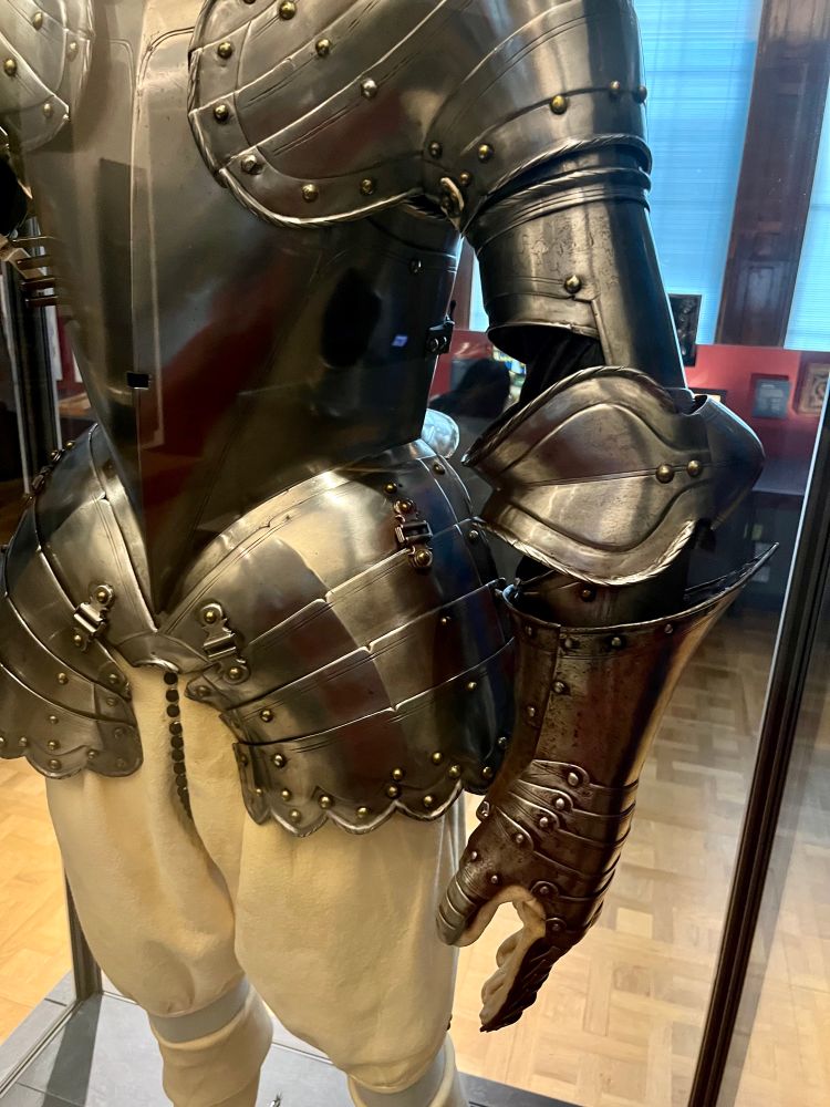 This half-armour was made for the tilt - a popular pastime for noblemen in about 1600, involving combat on horseback. Only the upper part of the body required protection. The breastplate had an attachment for a lance-rest and a reinforcing plate (grandguard) for the left shoulder. Underneath the armour a soft arming-doublet protected the skin from the hard metal and also provided some warmth. The illustration shows Charles, Prince of Wales (later Charles I) wearing a similar half armour.

Text from display 