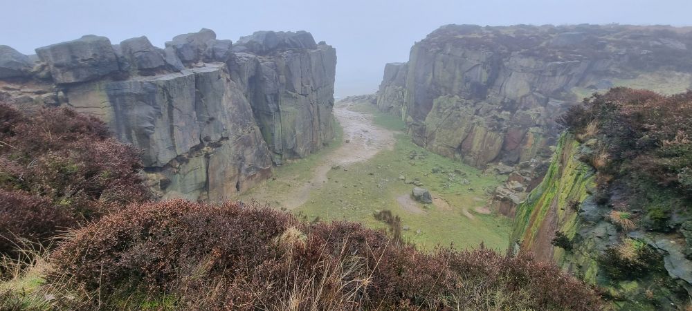 View of a gritstone quarry, from the top, where nothing can be seen beyond the rocks because of mist. Forefront of brown heather from the moor 