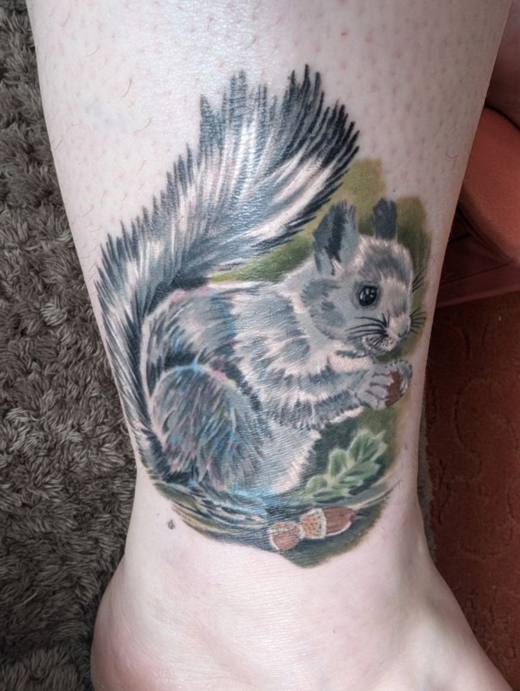 A photo of a woman's ankle with a tattoo of a grey squirrel eating acorns