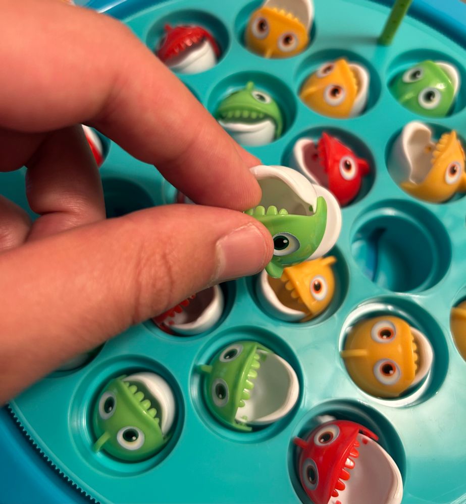 A hand putting a plastic fish into one of those mechanical rotating fishing games