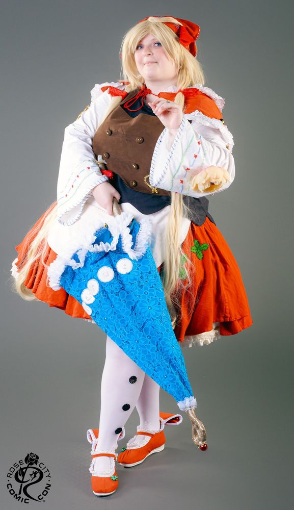 Minty Poison Cosplay wearing a costume of Polka from Eternal Sonata, holding a parasol across her front. Photo by Mahou Photos at their free photo booth.