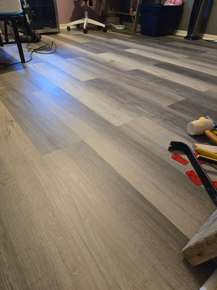 Newly-tiled bedroom floor, with pieces of furniture and tools on the perimeter. 
