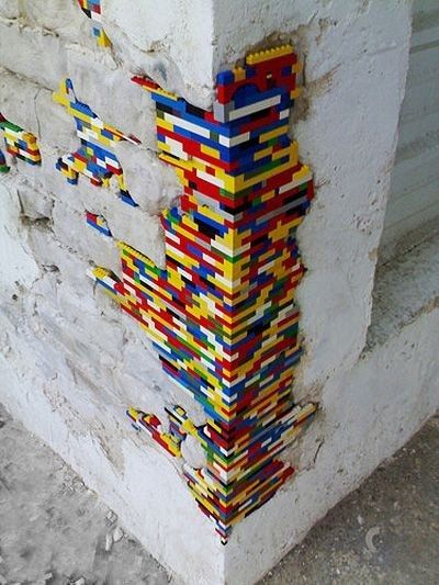 Angle d'un mur en pierre dont les parties manquantes sont comblées par un montage coloré de legos. Artiste : Jan Vormann