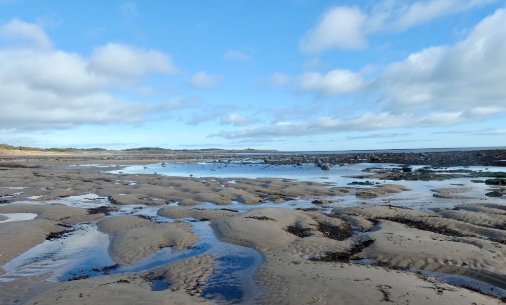 Blue sky, light clouds, rocks sea and sand.
