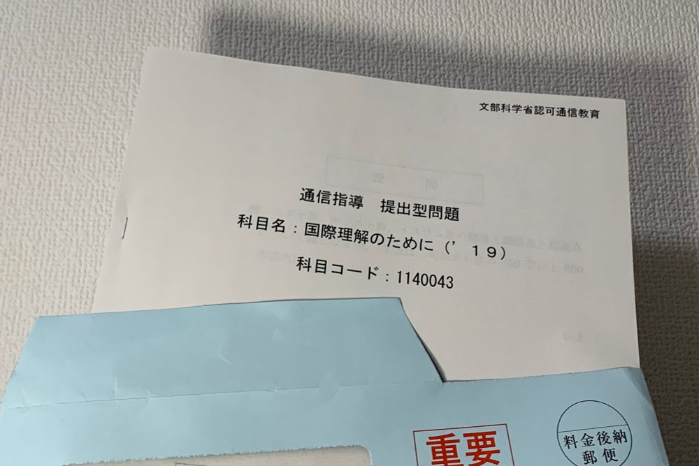 青い封筒から上半分だけ取り出された書類の写真。
書類の中央には「通信指導 提出型問題」「科目名：国際理解のために("19) 科目コード：1140043」と書かれている。
書類右上には小さく「文部科学省許可通信教育」の文字がある