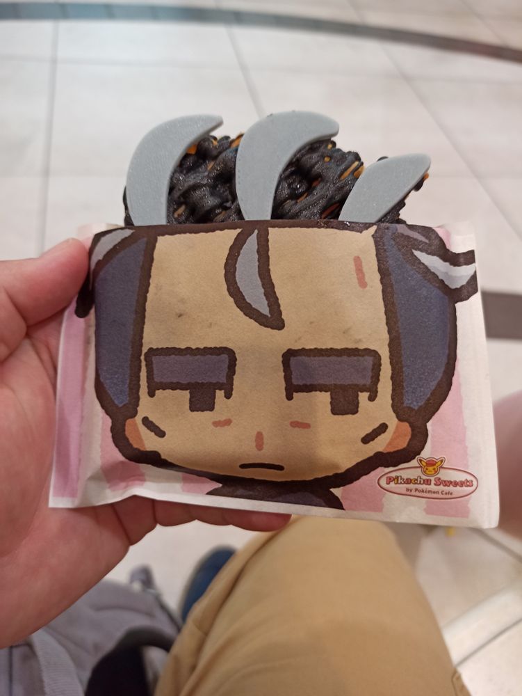 Photograph of the Pokémon Sweets Cafe Larry style waffle, with icing chunks representing his grey hair, and a paper cover with a chibi version of his face on it