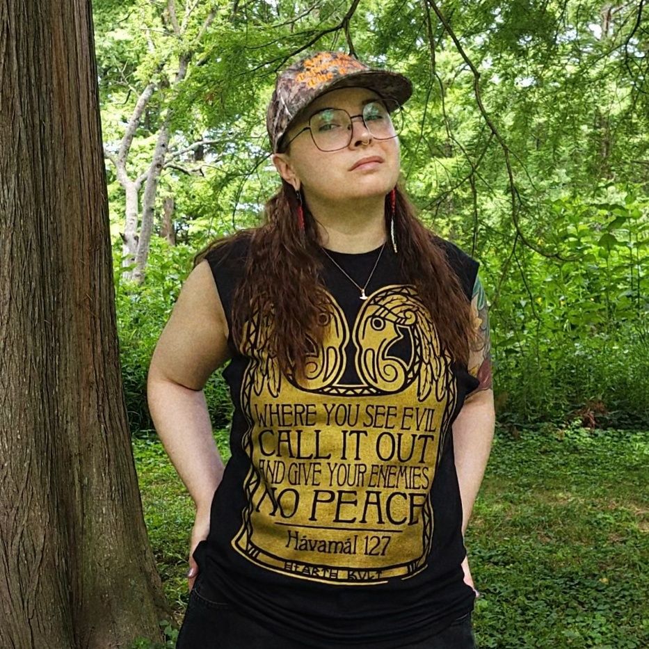photo of me in a very green park. i'm wearing a black t-shirt with a golden-inked graphic, featuring a plaque with two raven heads and "WHERE YOU SEE EVIL, CALL IT OUT, AND GIVE YOUR ENEMIES NO PEACE" - which comes from stanza 127 of the Hávamál.
